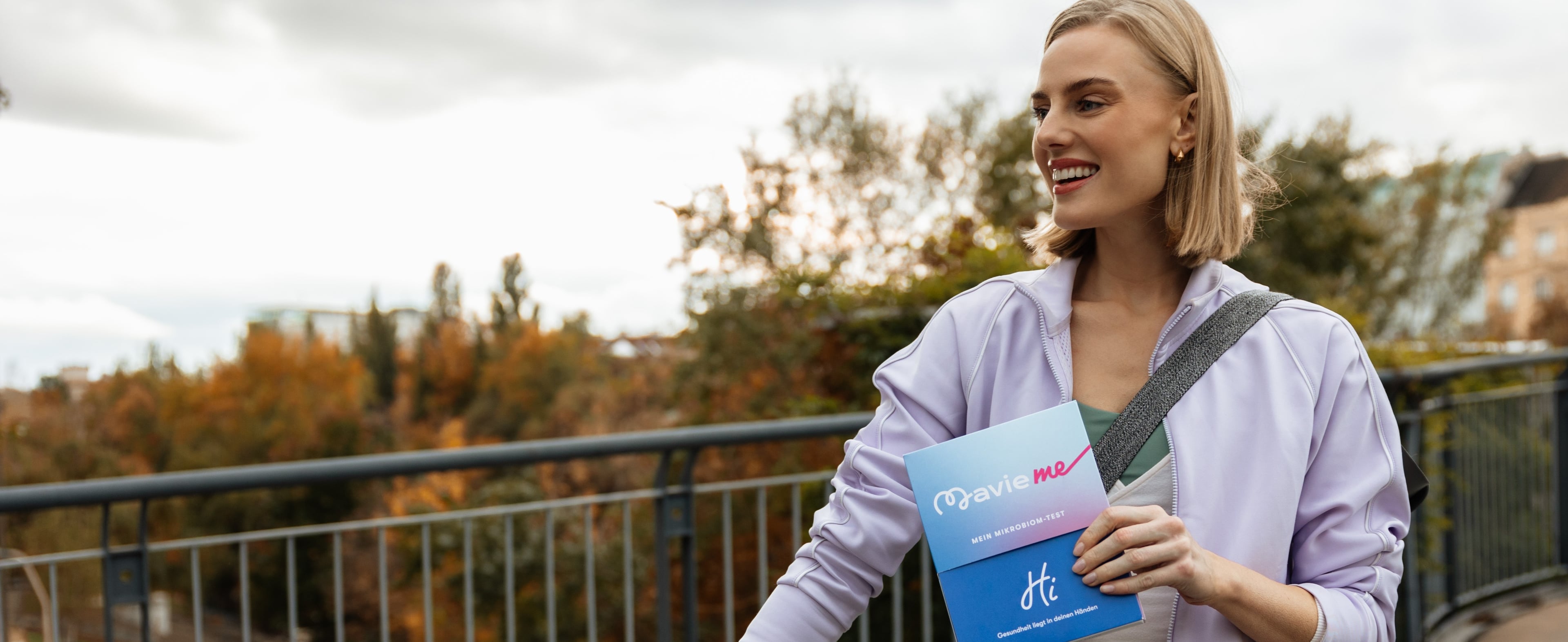 Woman standing beside a bicycle outdoors while holding a MavieMe microbiome test kit, promoting preventive health and an active lifestyle.
