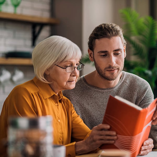 Older woman reading a book together with a younger man – symbol of active ageing and excellent care at home.