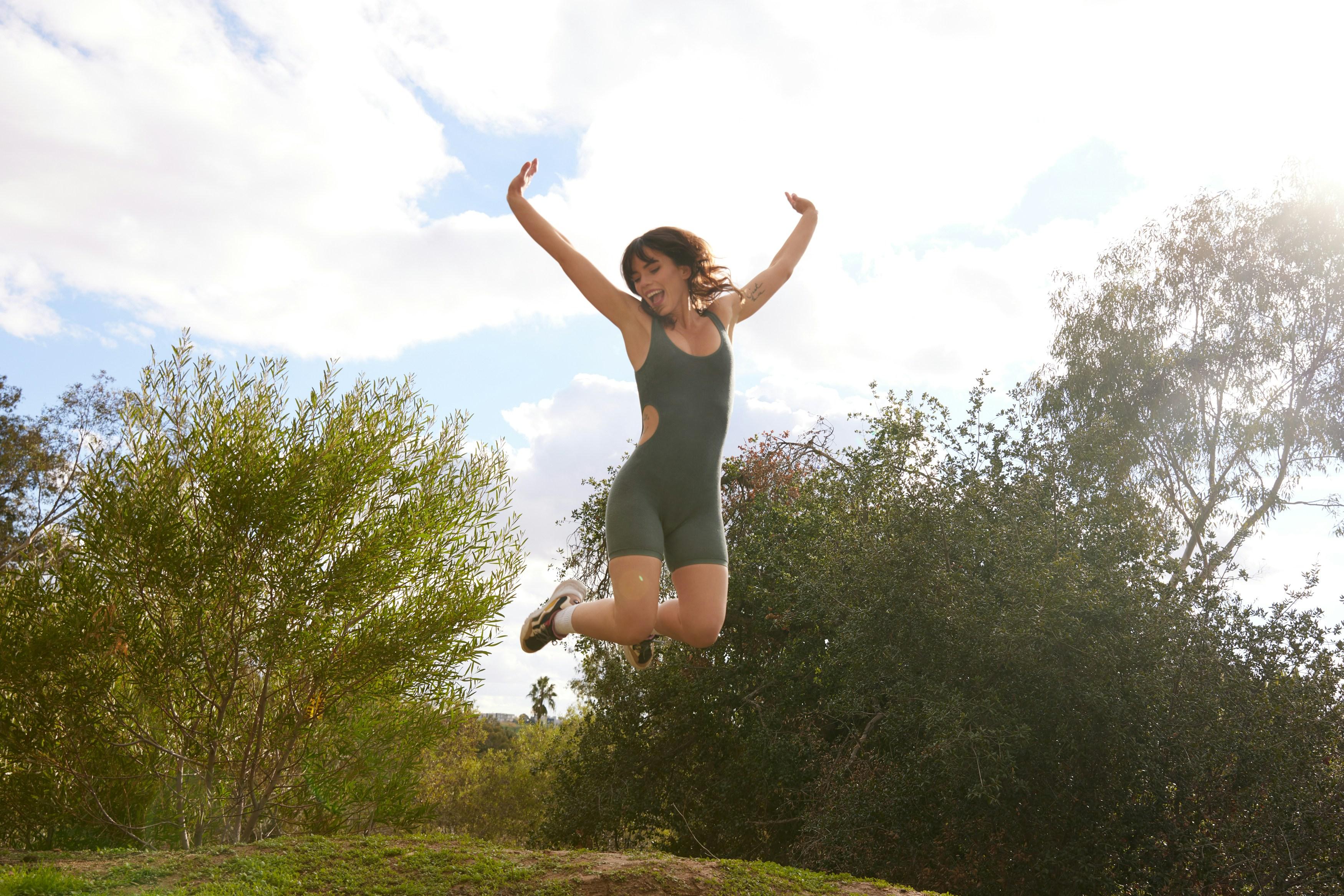 3 Innovative Health Projects in Vienna You Should Know About Young woman in athletic wear joyfully jumps into the air, surrounded by trees and bright daylight – a moment of energy and vitality.