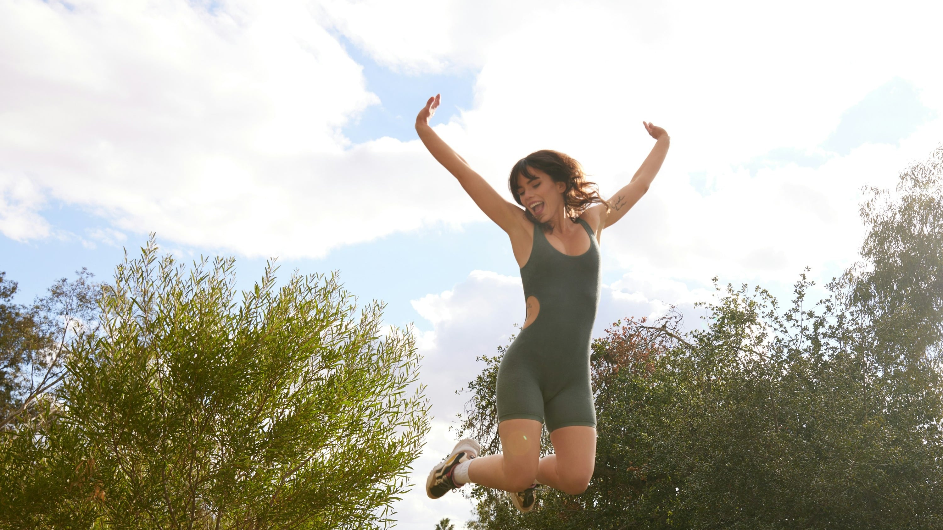 Young woman joyfully jumps into the air in athletic wear, surrounded by trees and bright daylight—capturing a sense of energy and joy for life.