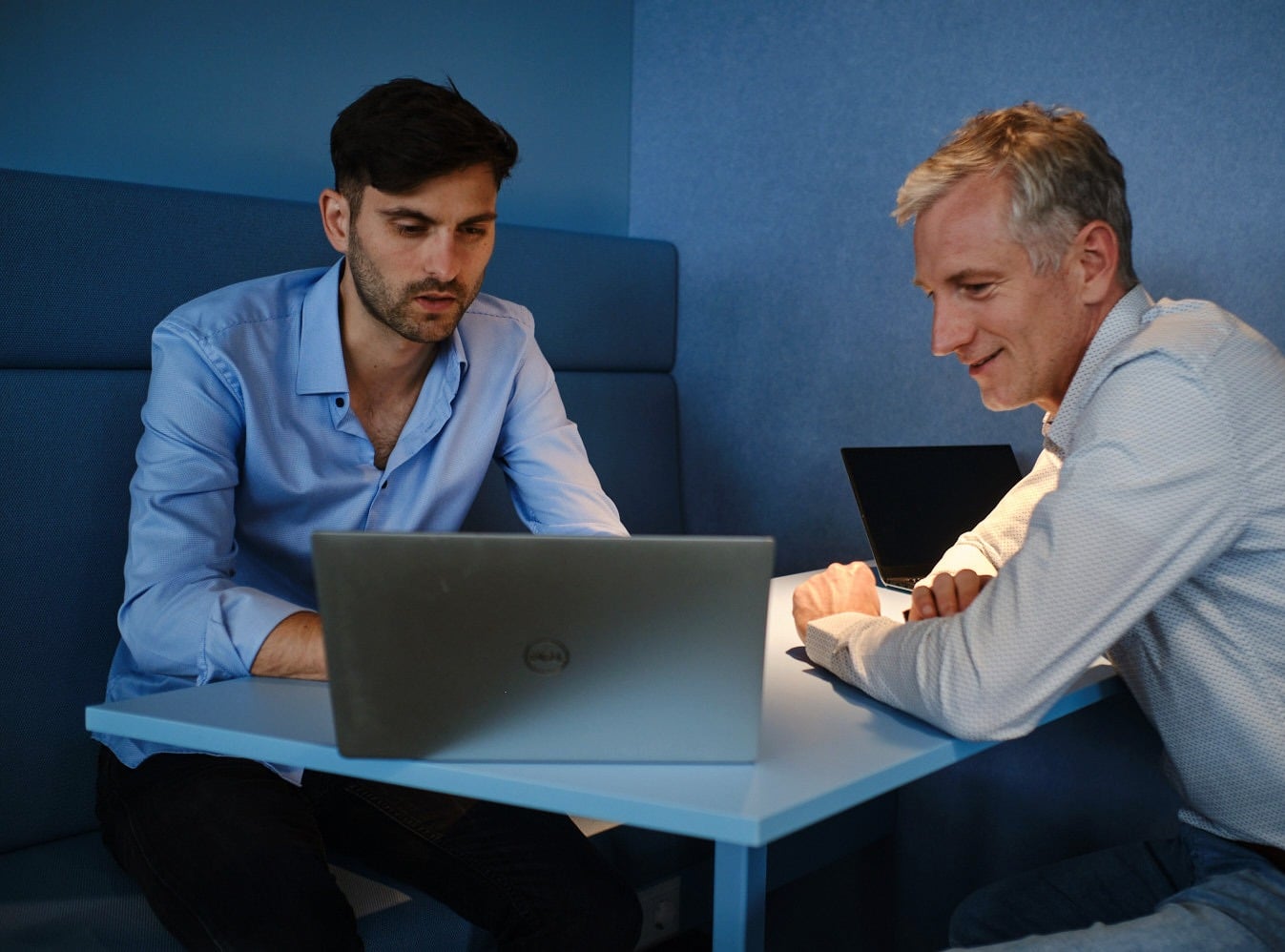 Two colleagues working together on a laptop in a modern office meeting booth.
