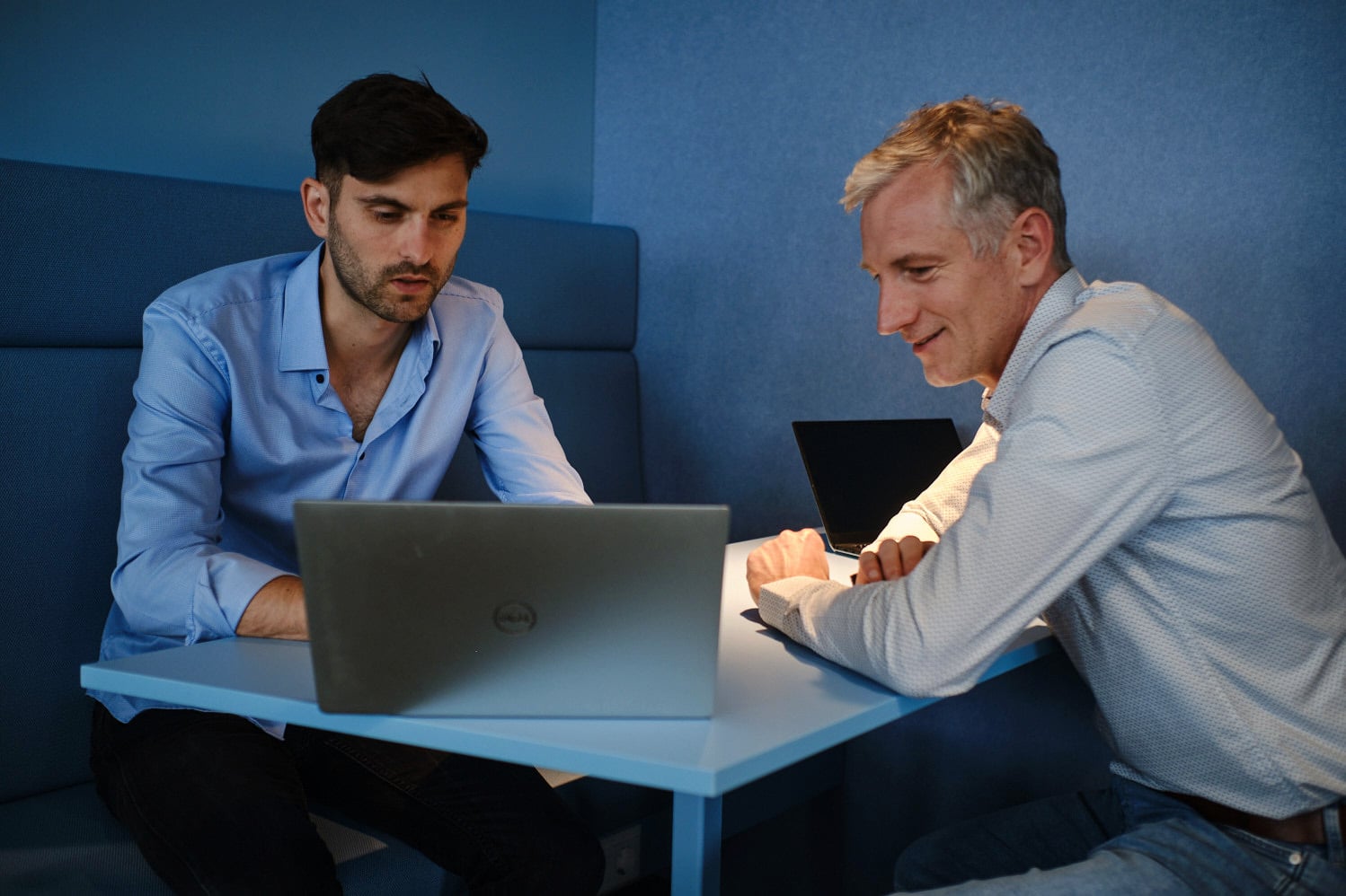 Two colleagues working together on a laptop in a modern office meeting booth.