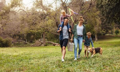 Family with two children and a dog walking in the park – symbolic image for health, prevention, and an active family lifestyle