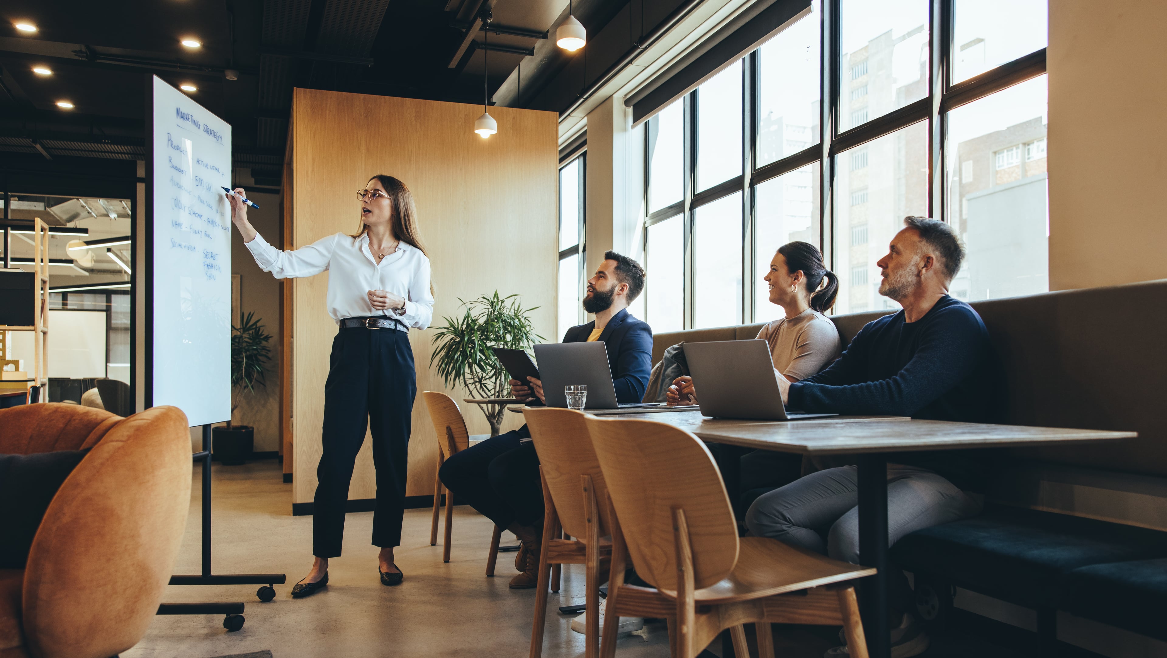Woman presenting information on a whiteboard while colleagues listen attentively in a modern meeting room.
