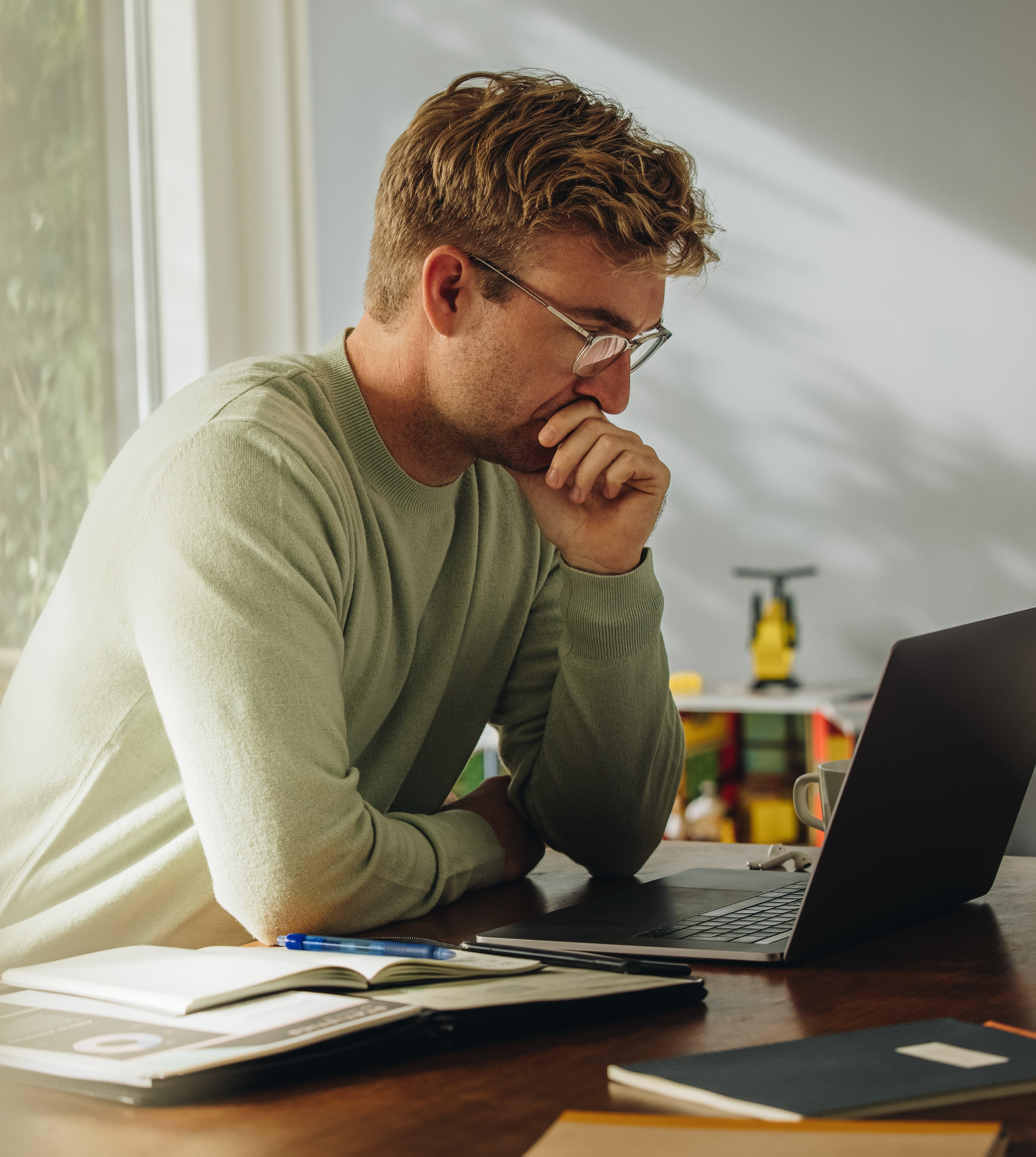 Mann sitzt nachdenklich am Schreibtisch und arbeitet an einem Laptop im Homeoffice.