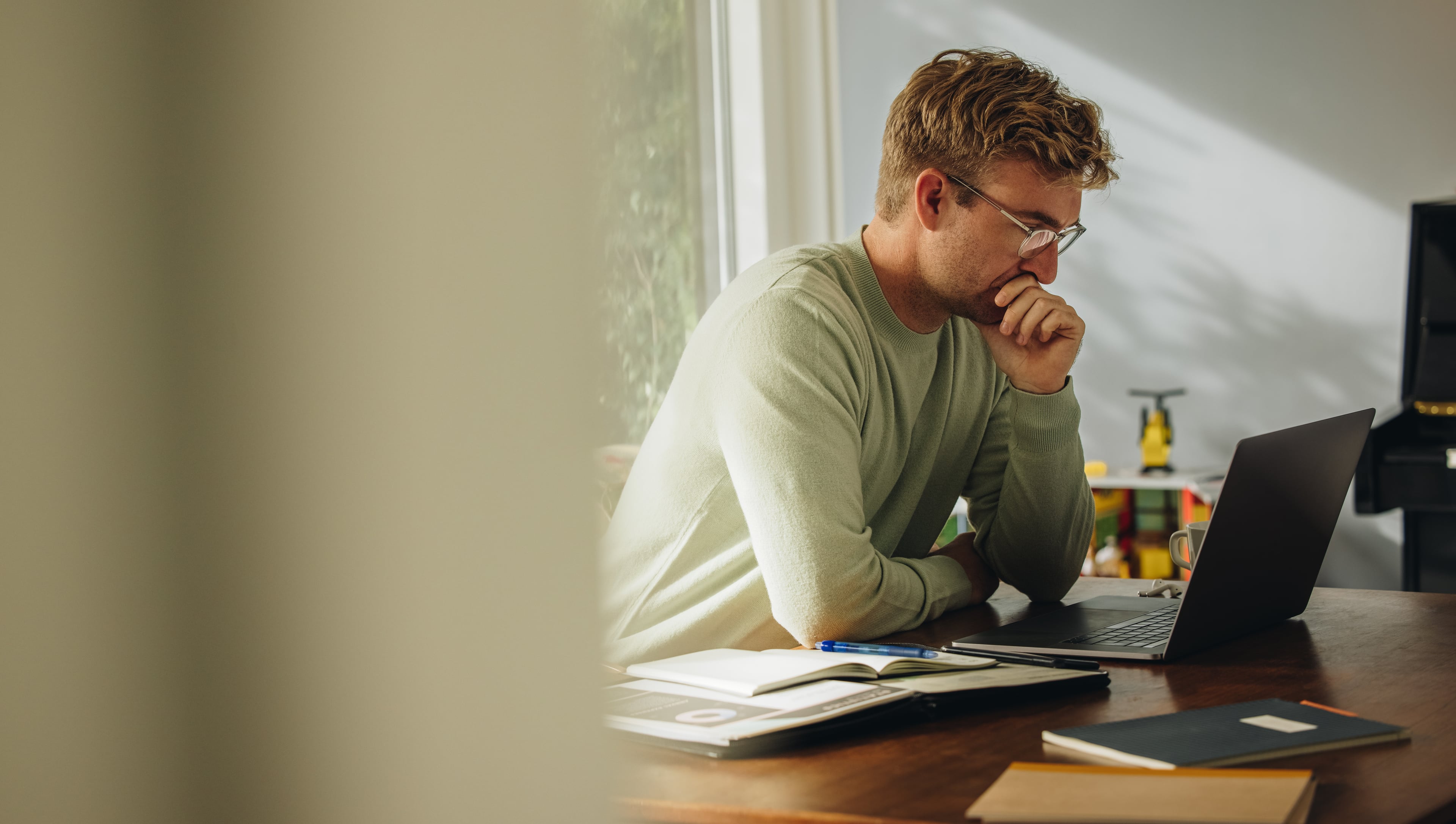Man sitting at a desk working on a laptop in a focused home office setting.