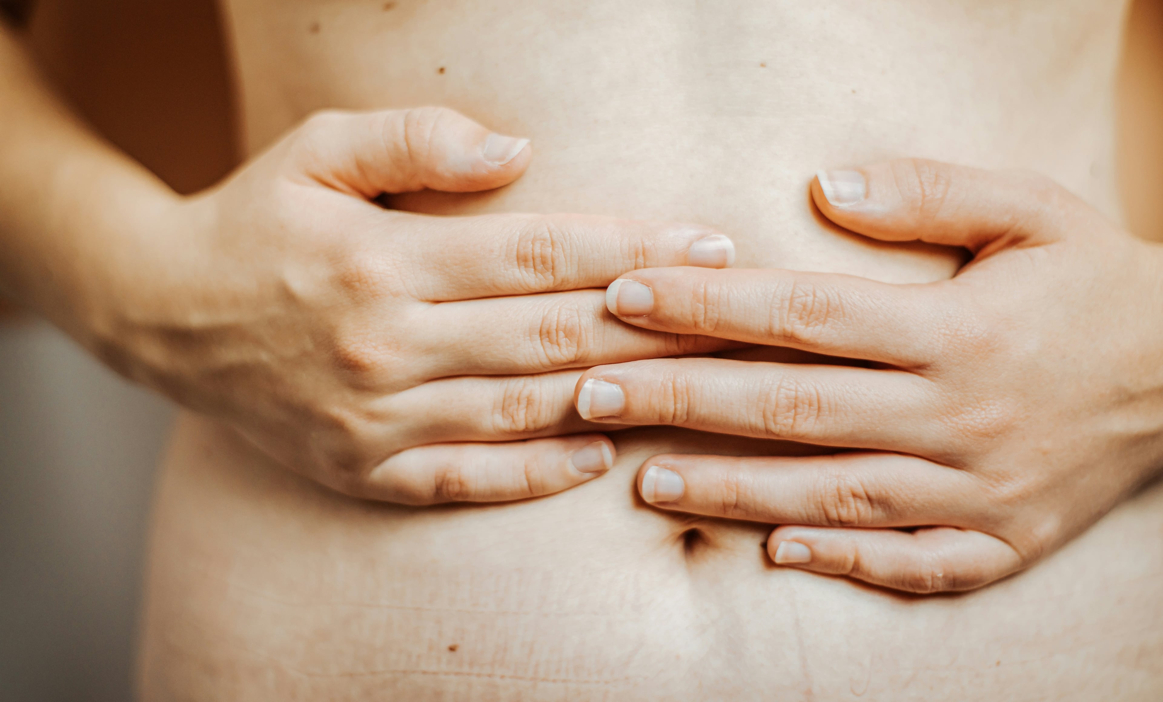 Close-up of a person placing both hands on their abdomen.