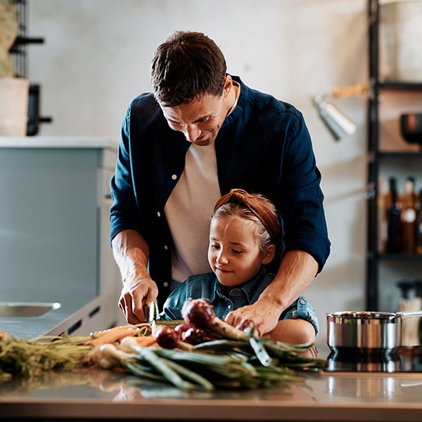 Vater kocht gemeinsam mit seiner Tochter frisches Gemüse in der Küche – Symbol für gesunde Ernährung und Prävention.