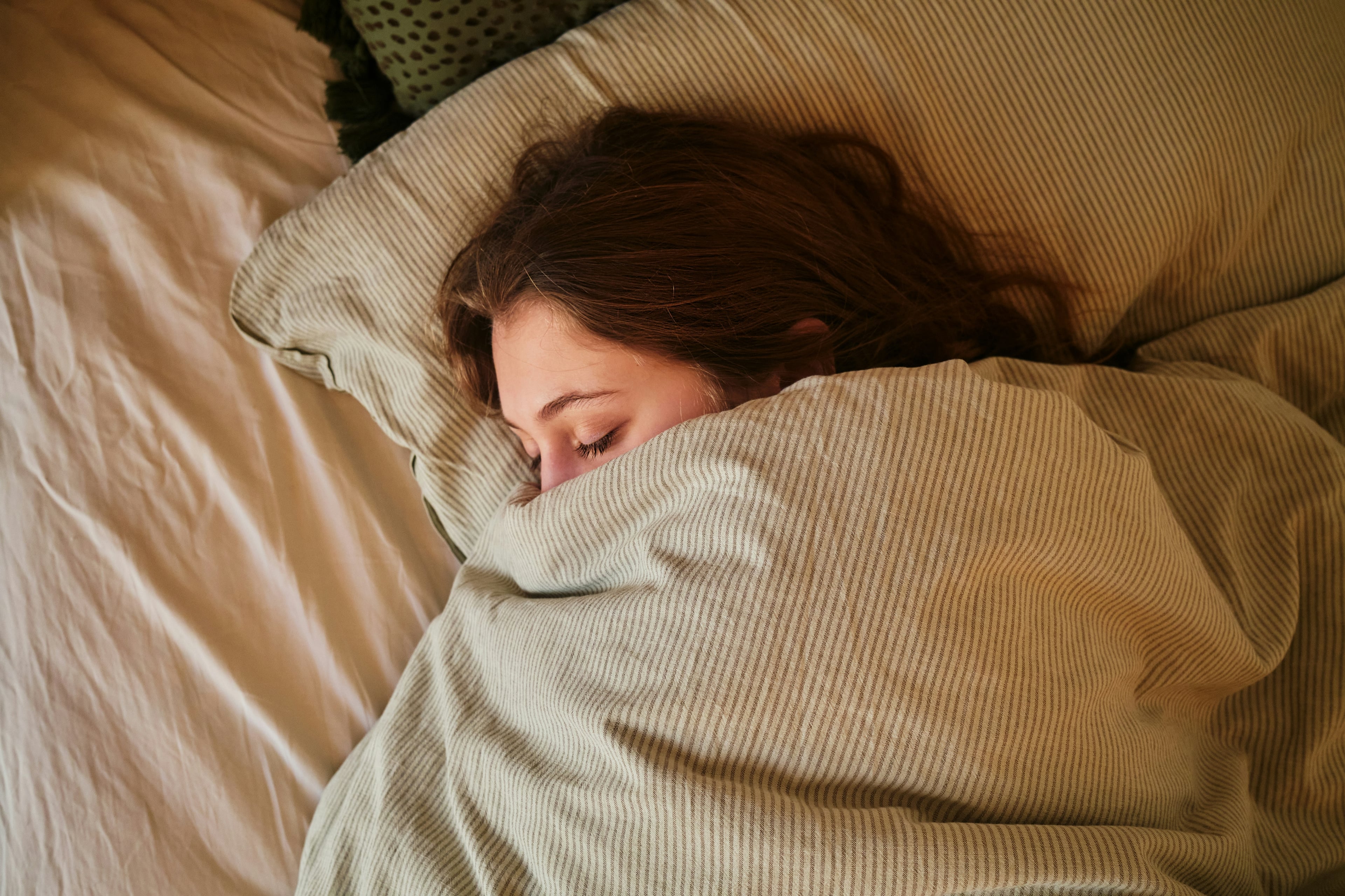 Person schläft zugedeckt in einem Bett mit Kopf auf einem Kissen.