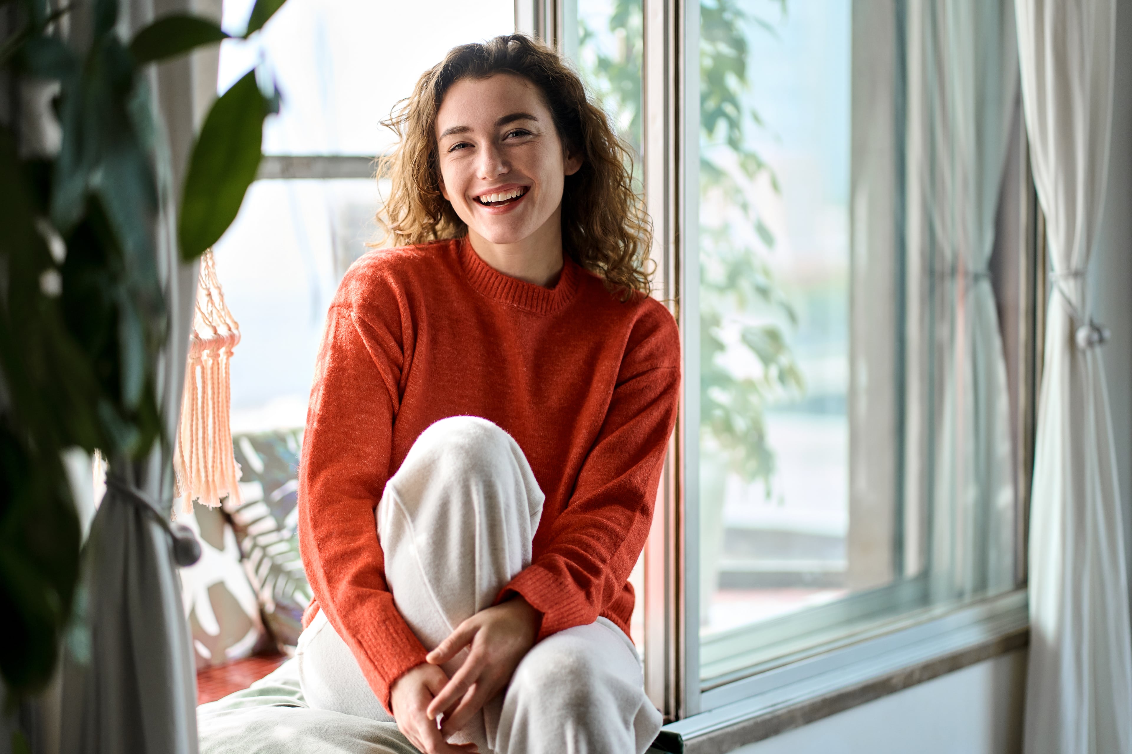 Smiling young woman sitting by a window at home and enjoying a calm and peaceful moment.