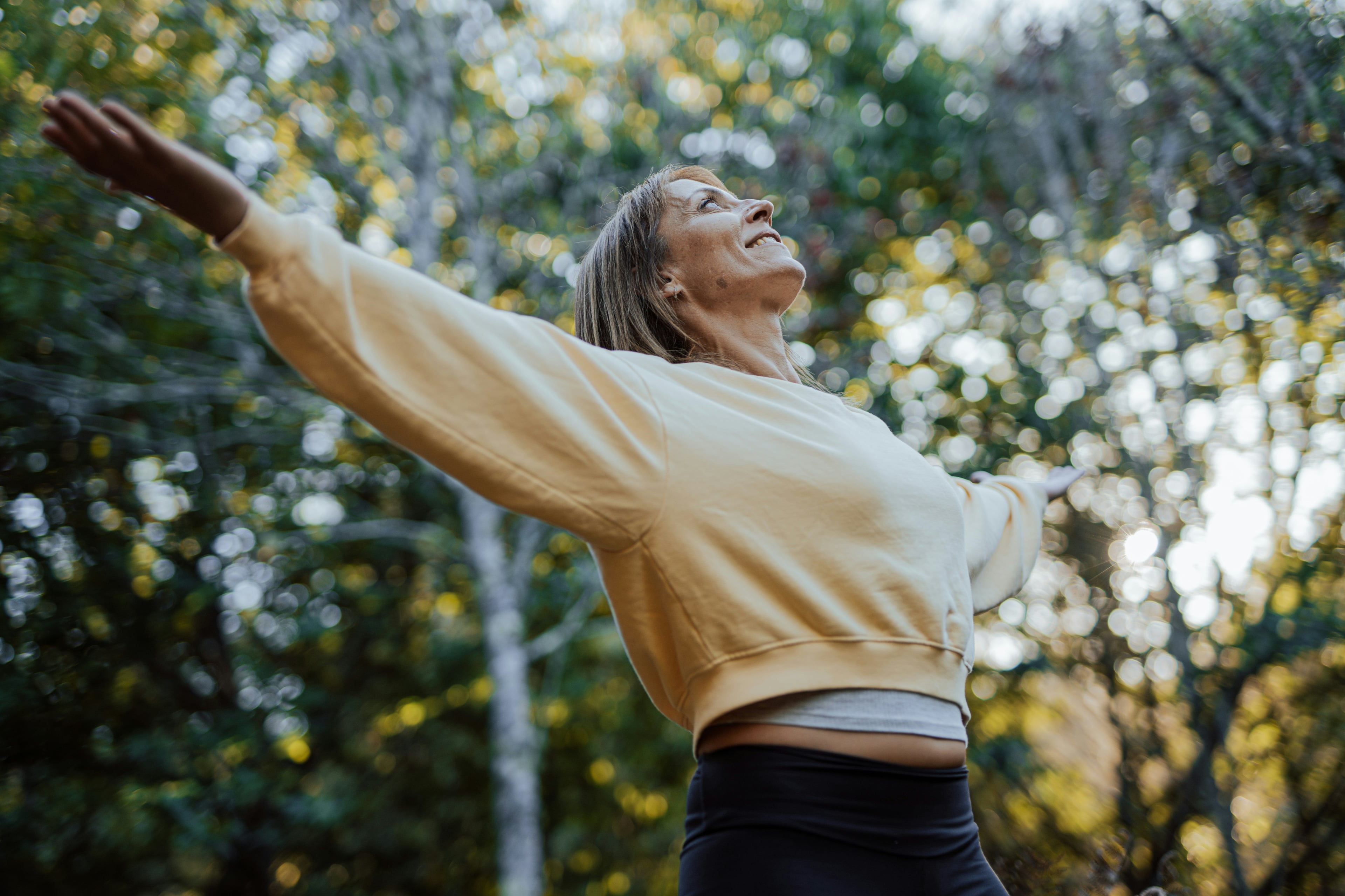 Woman with outstretched arms in a forest, enjoying a moment of movement, relaxation and wellbeing in nature.
